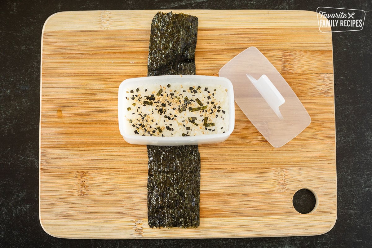 Cutting board with sesame topping on sushi rice in a musubi mold.
