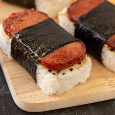 Homemade Hawaiian Spam Musubi on a wooden cutting board, showcasing layers of rice, Spam, and nori roasted seaweed.