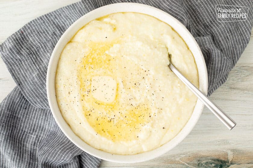 Spoon resting in a bowl of Grits with melted butter and pepper.