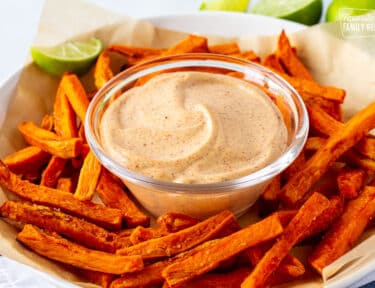 Plate of sweet potato fries with dipping sauce in the center.