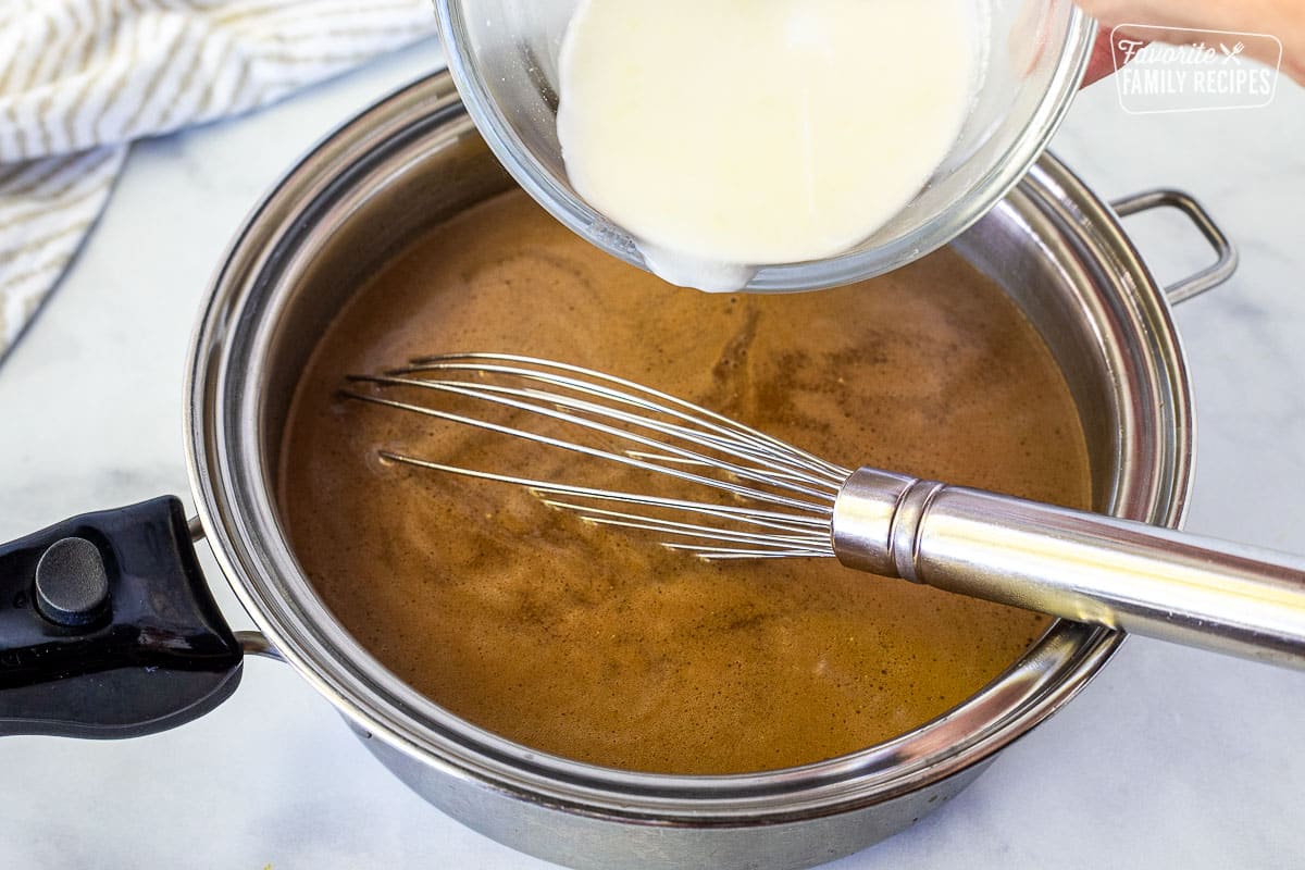 Pouring cornstarch mixture into saucepan of beef broth. Whisk resting in saucepan.