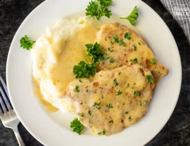 Two Crock Pot Pork Chops on a plate with mashed potatoes and gravy.
