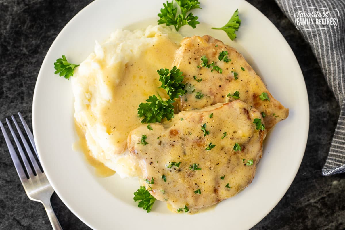 Fork-tender crock pot pork chops with creamy gravy on a plate, easy dinner recipe when served over mashed potatoes.