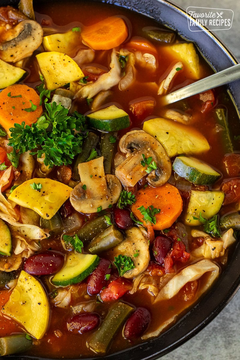 Bowl of Weight Loss Soup filled with zucchini, mushrooms, carrots, onions, cabbage, and green beans with a spoon.