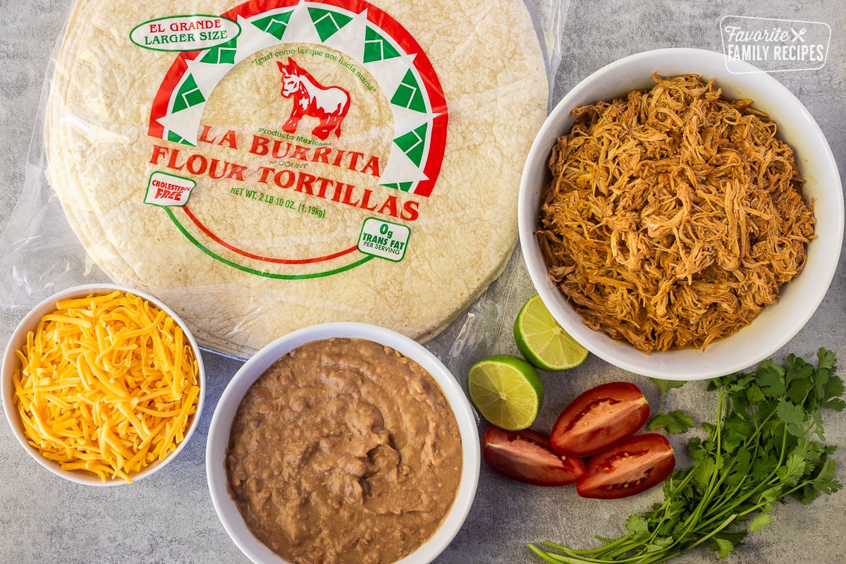 Ingredients to make Chicken Chimichangas including extra large tortillas, Mexican shredded chicken, refried beans, cheese, cilantro, lime and tomatoes.