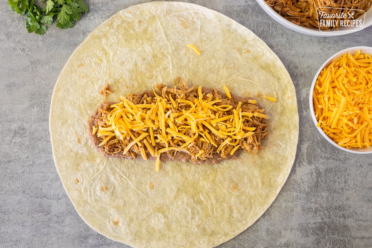 Cheddar cheese on top of chicken and refried beans on a flour tortilla.