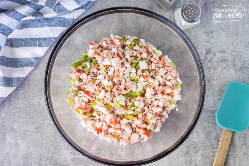 Glass mixing bowl with cut up crab and celery. Spatula on the side.