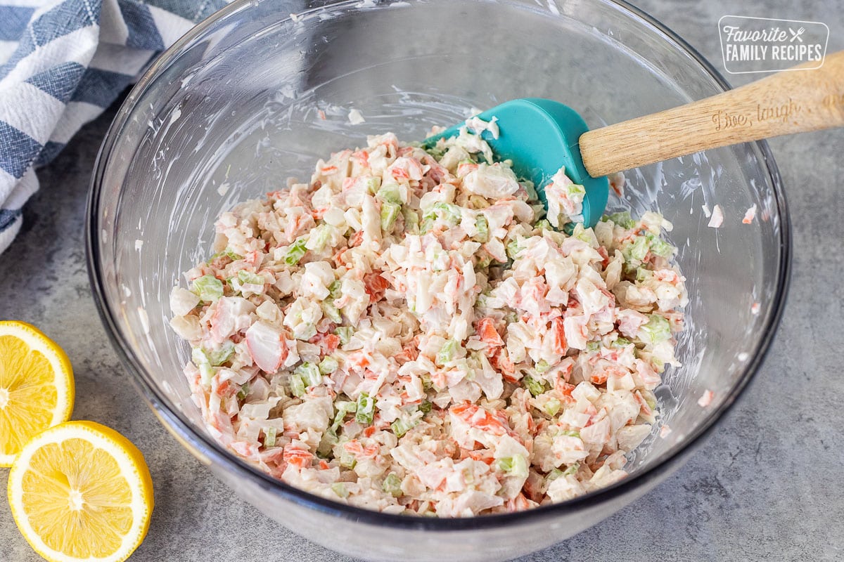 Mixing crab salad in a glass mixing bowl with a spatula.