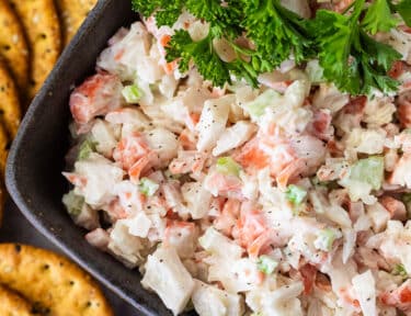 Cold Crab Dip in a bowl with parsley on top and crackers on the side.