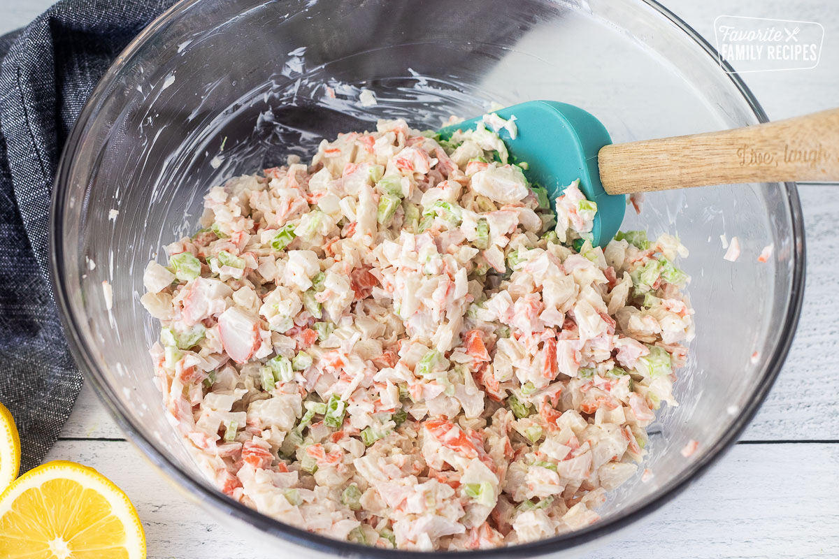 Stirring crab salad with a spatula in a glass mixing bowl.