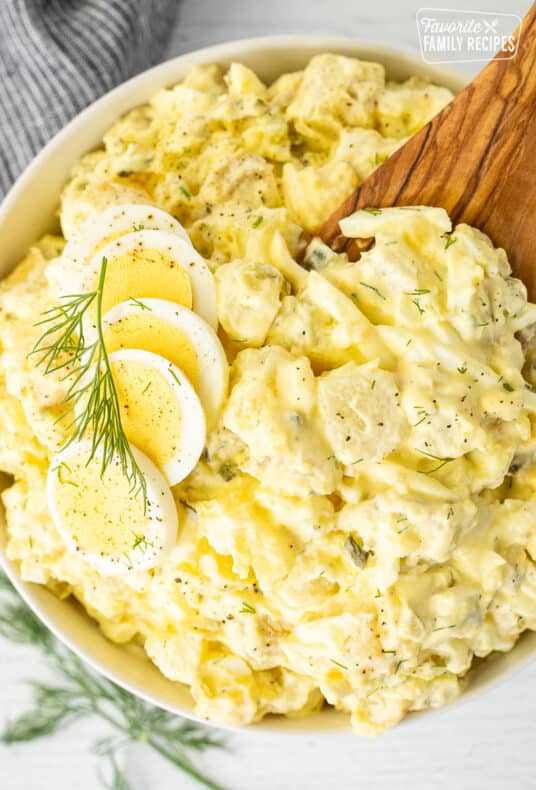 Wooden spoon resting in a bowl of Homemade Potato Salad.