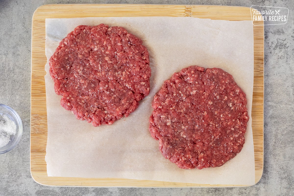 Two flattened ground beef patties on parchment paper.