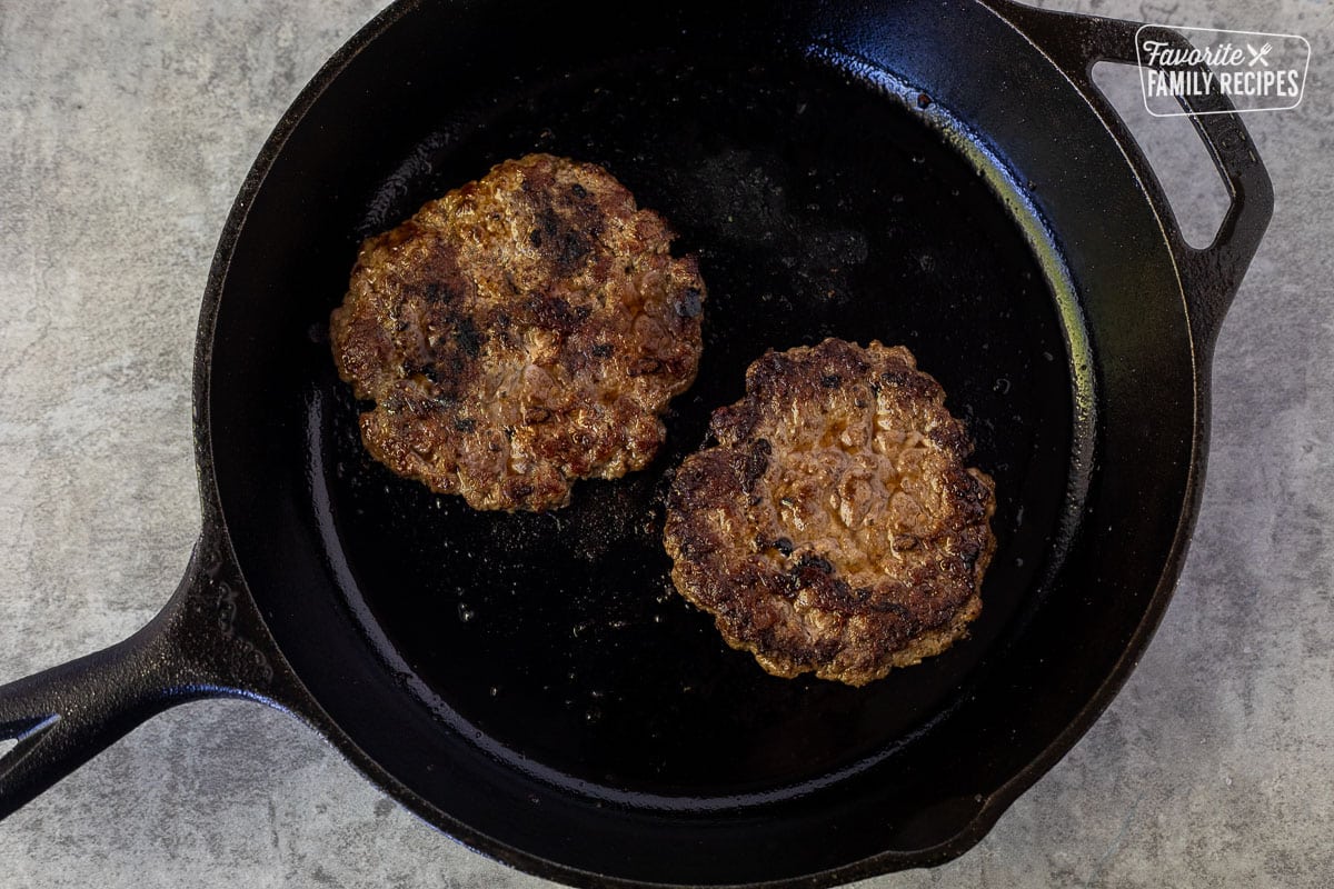 Skillet with two browned ground beef patties.