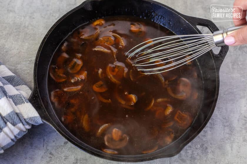 Stirring beef gravy in a skillet with a whisk.