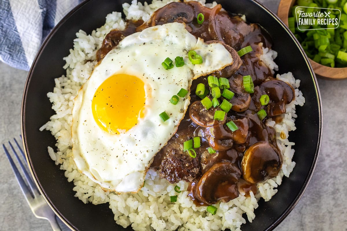 Loco Moco in a bowl with rice, beef patty, gravy, mushrooms, egg and green onion.