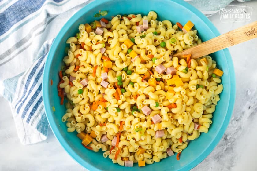 Mix of pasta and mix ins in a large bowl with a wooden spoon.