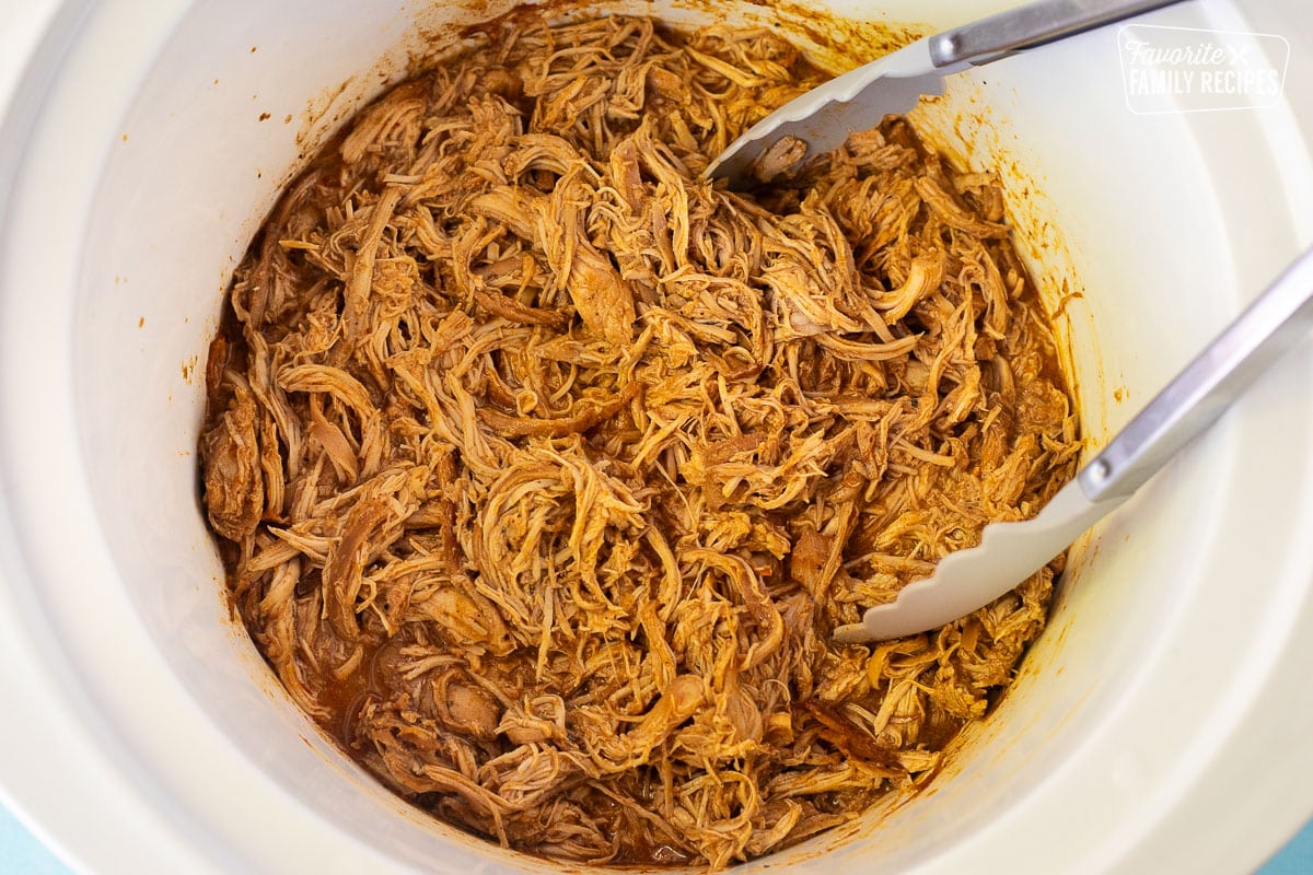Mexican Shredded Chicken in crockpot with tongs.