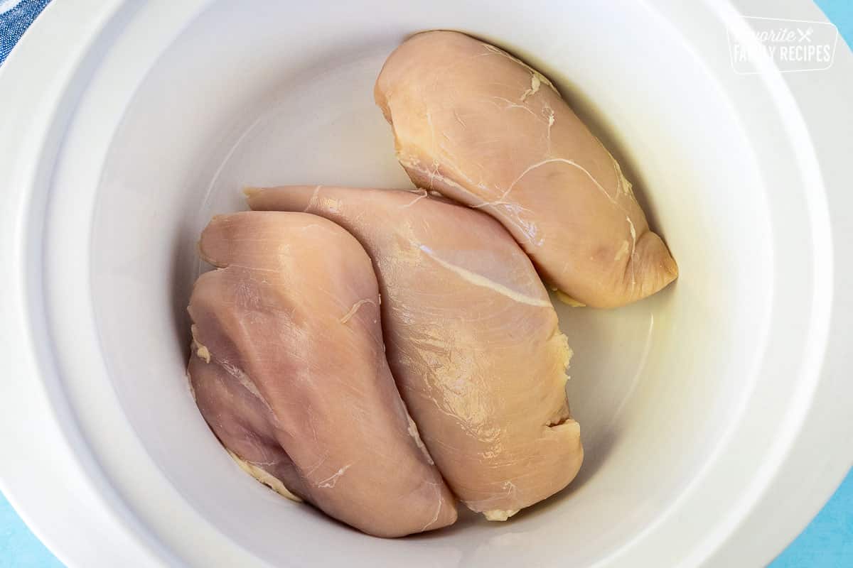 Crock pot with three chicken breasts.