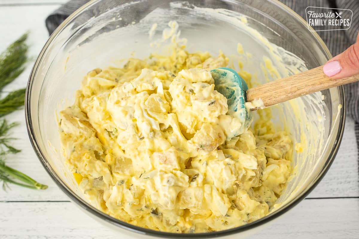 Stirring potato salad with a spatula in a glass bowl.