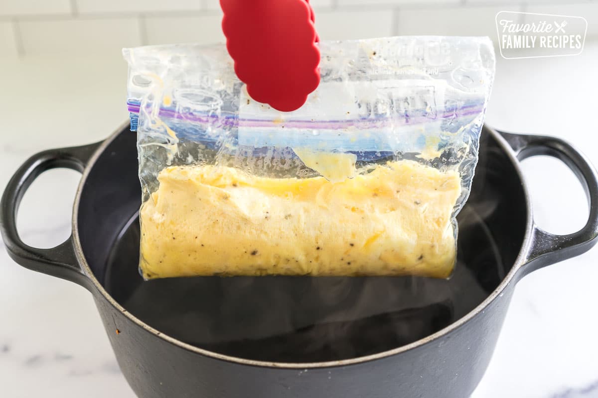 tongs pulling a ziplock bag with cooked eggs out of a pot of water
