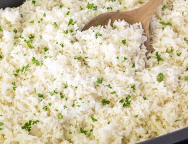Cooked rice in a roasting pan with parsley as garnish. Wooden spoon in the pan.