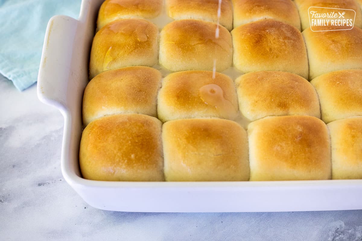 A coconut mixture being poured over hot rolls for Pani Popo coconut rolls.