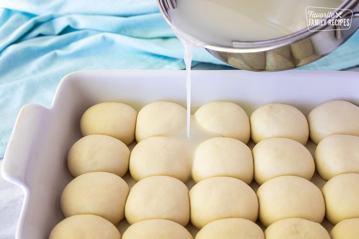 Pouring coconut mix from a saucepan onto risen dinner rolls for Pani Popo recipe.