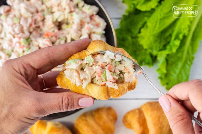 Stuffing crab salad in a croissant with a spoon.