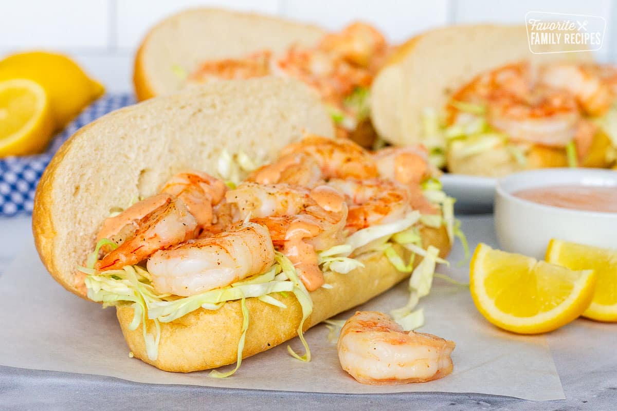Three Shrimp Po'Boy Sandwiches with a cajun sauce and fresh lemon wedges.
