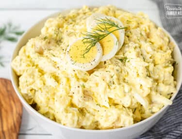 Bowl of Homemade Potato Salad with sliced hard boiled eggs on top and fresh dill.