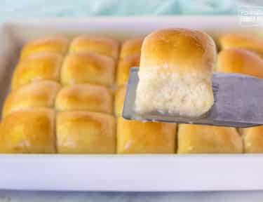 Spatula holding up a single Pani Popo roll over a pan of Samoan Coconut rolls.