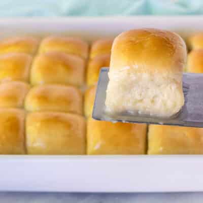 Spatula holding up a single Pani Popo roll over a pan of Samoan Coconut rolls.