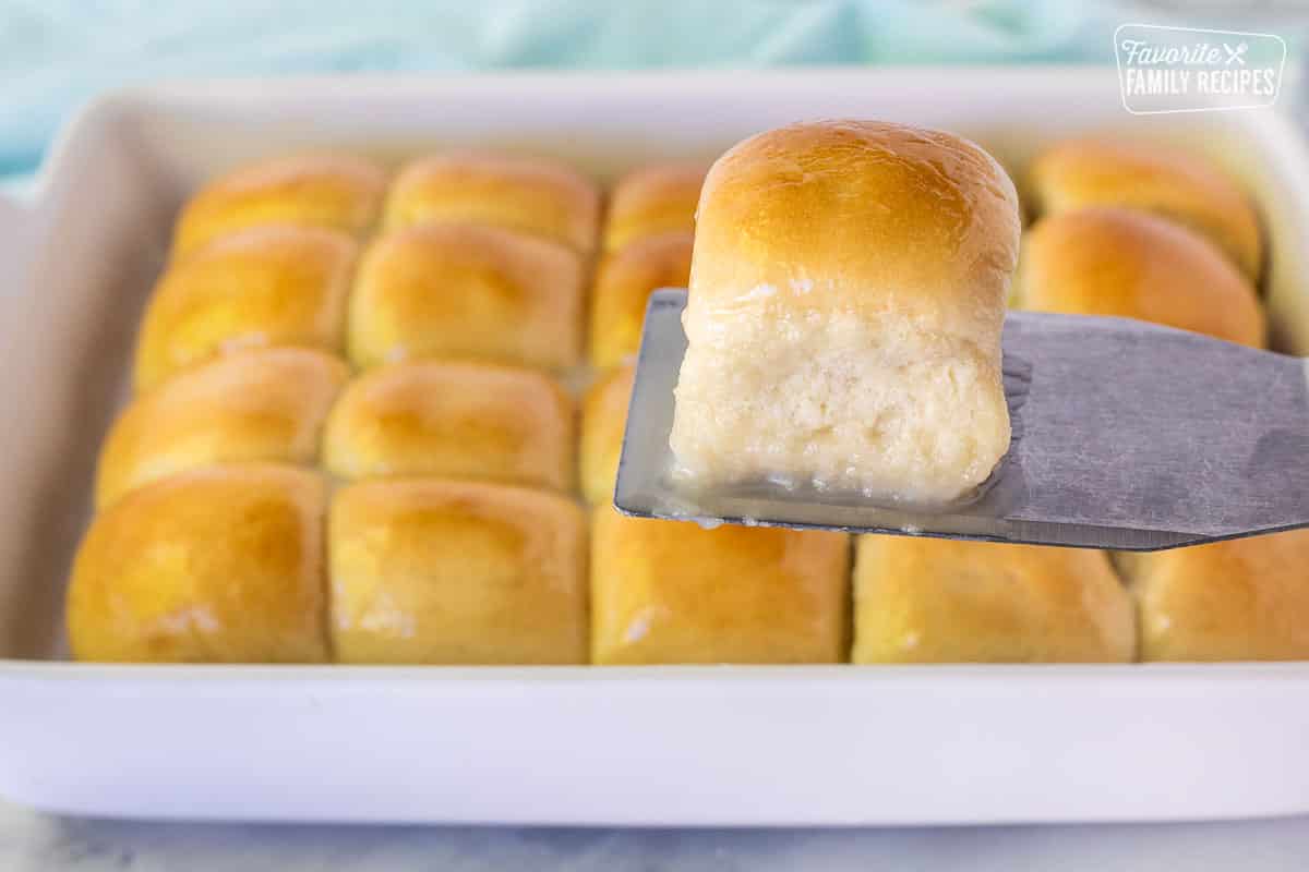 Spatula holding up a single Pani Popo roll over a pan of Samoan Coconut rolls.