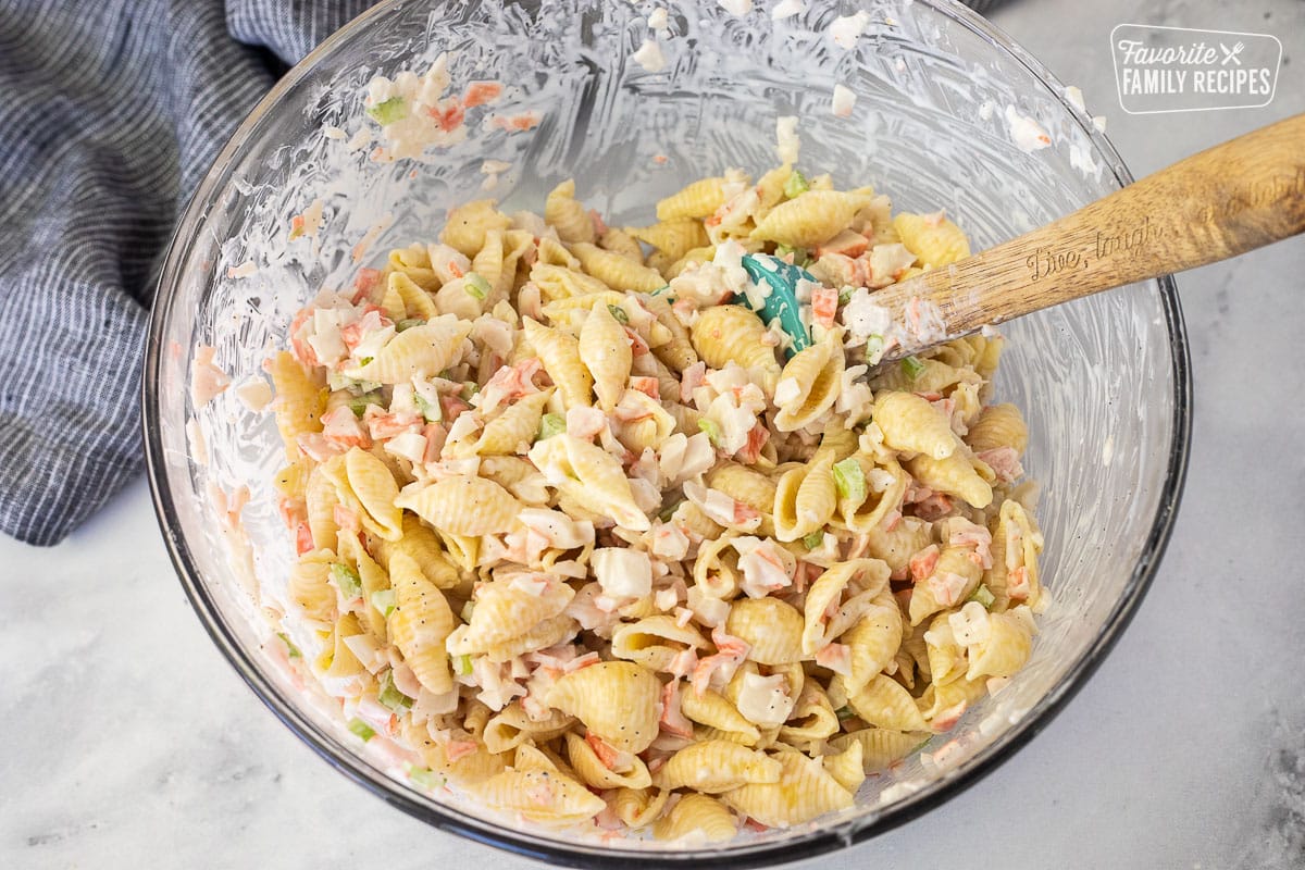 Mixing crab mixture with pasta in a glass bowl with a spatula.