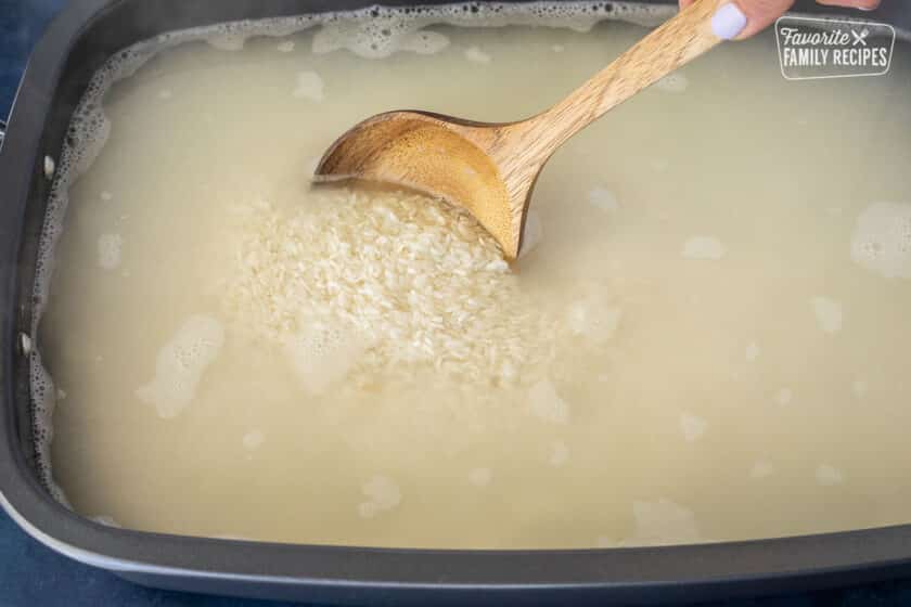 Stirring hot water into roasting pan with rice.