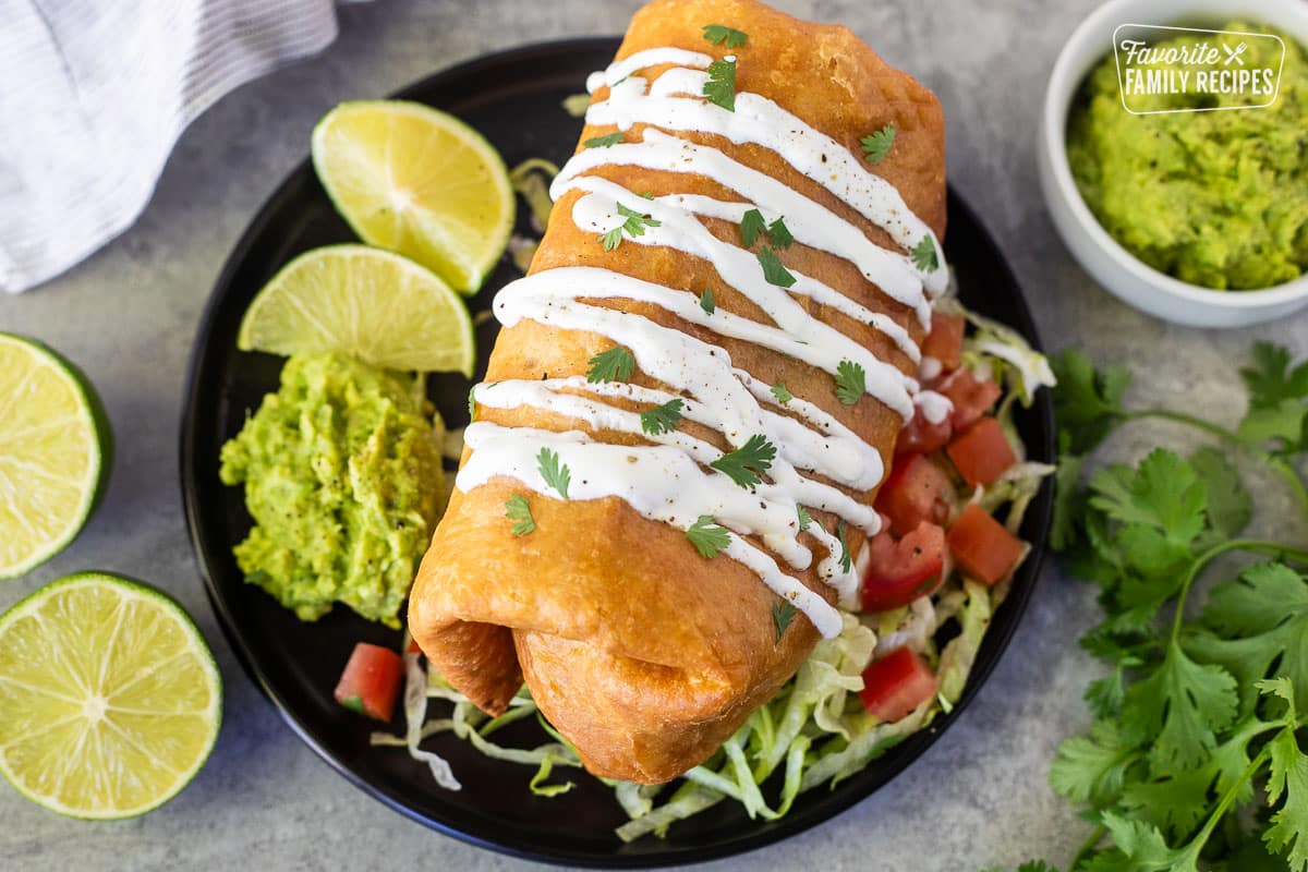 Chicken Chimichanga with sour cream drizzled on top and cilantro resting on a plate with lettuce, tomatoes and guacamole.