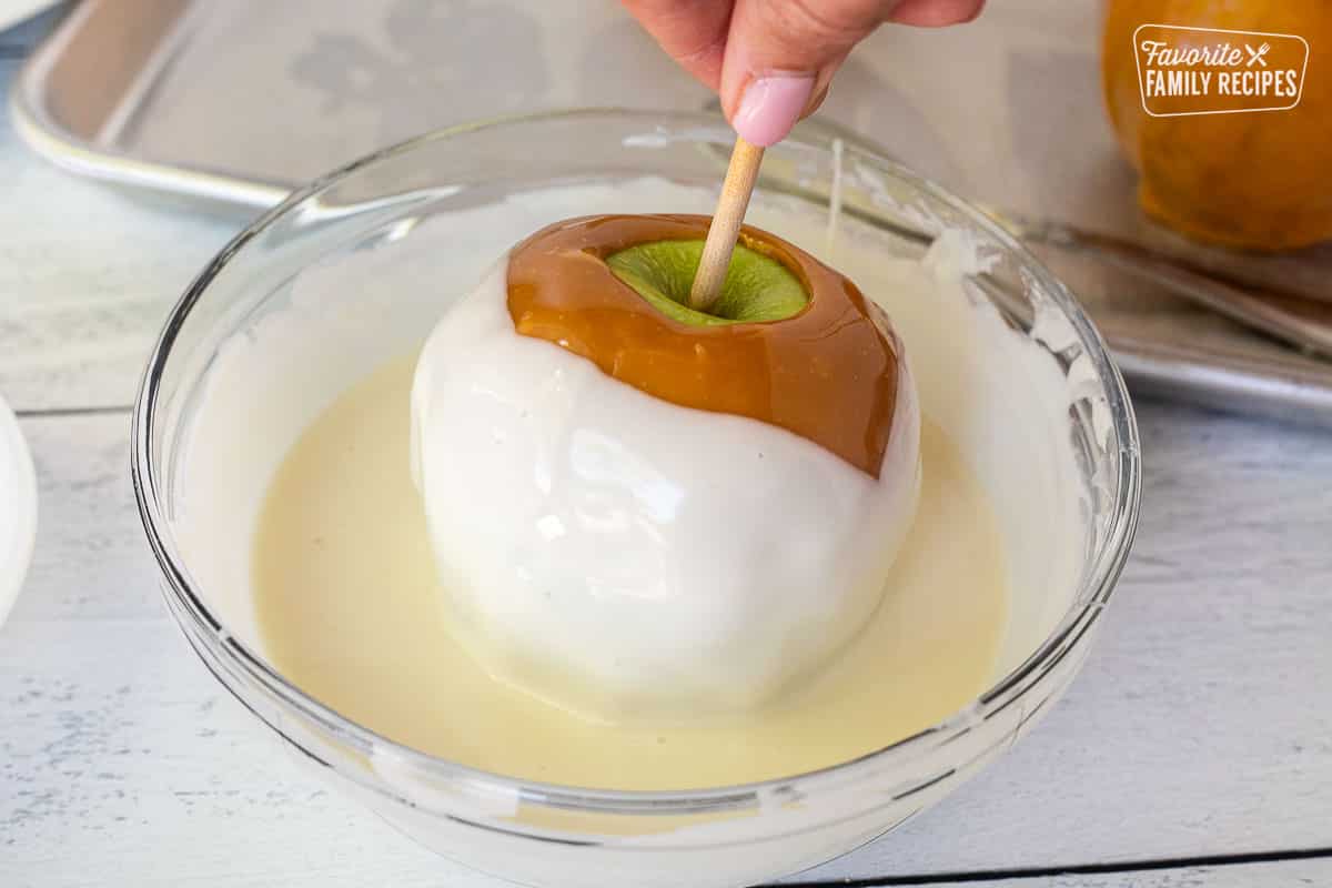 Dipping caramel apple into a bowl of melted white chocolate.
