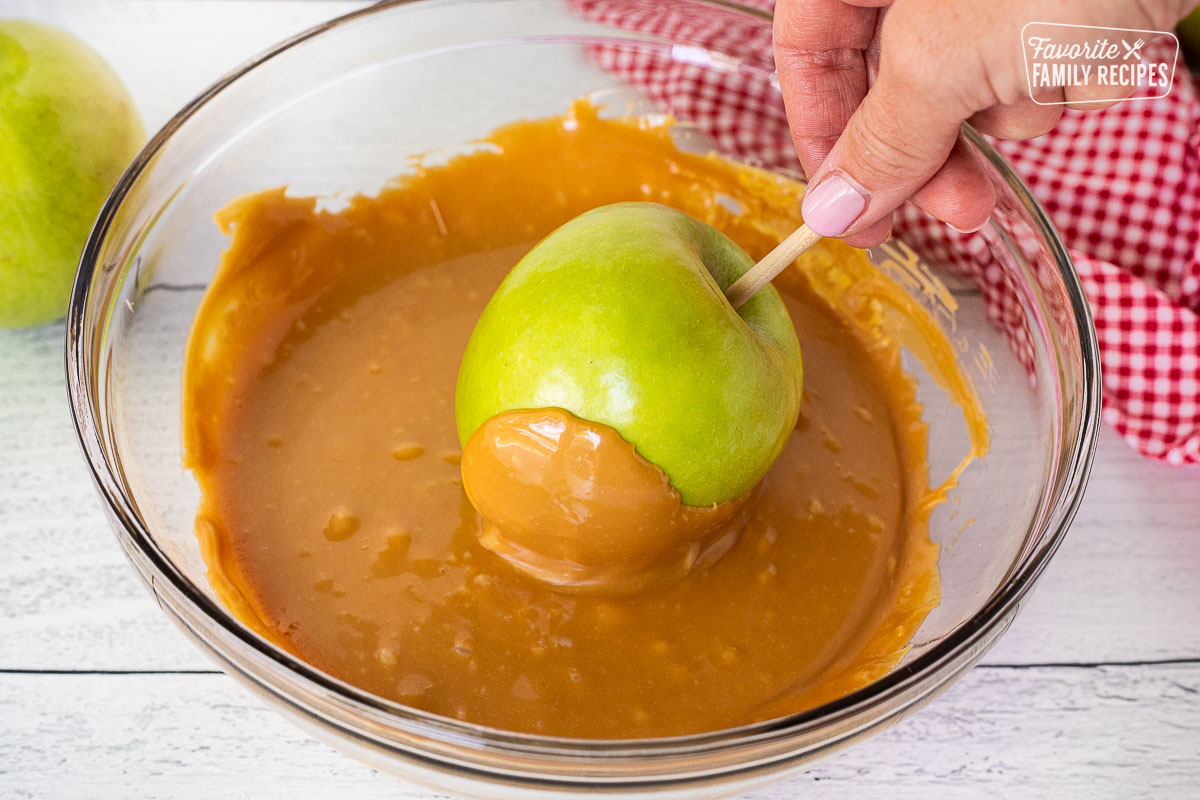 Dipping a green apple into bowl of melted caramel.