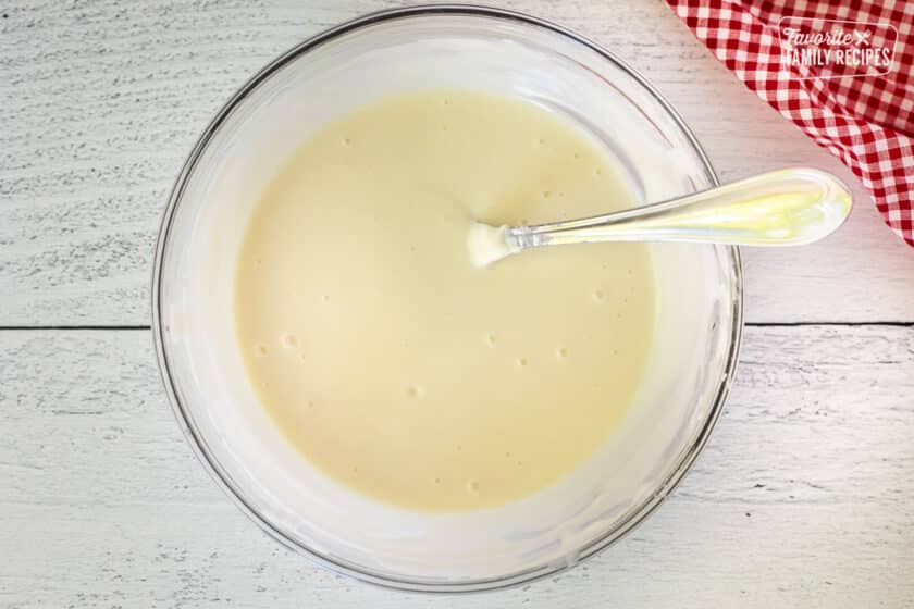 Glass mixing bowl with white melted chocolate and a spoon.