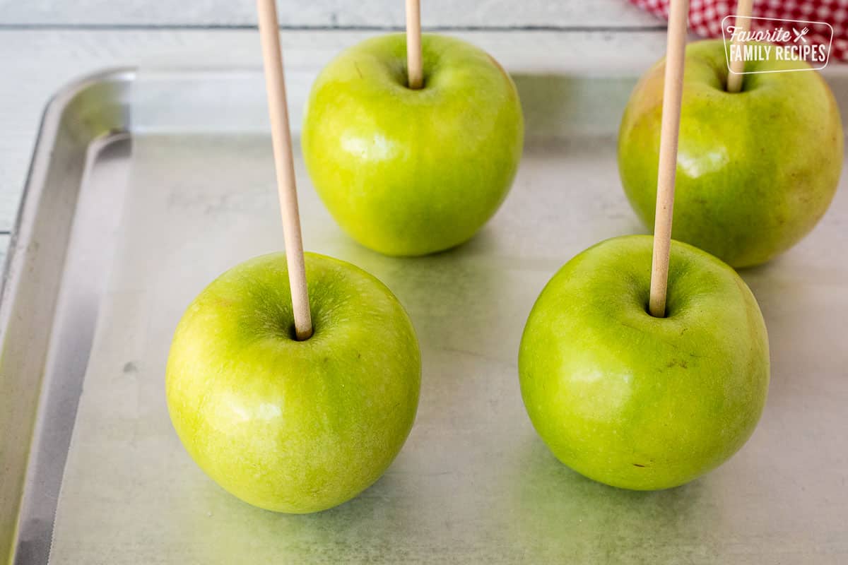 Four green apple with wooden sticks stabbed on top.