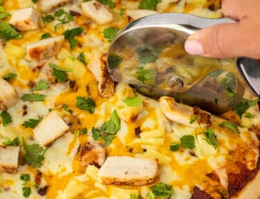 Cutting BBQ Chicken Pizza with a pizza cutter.