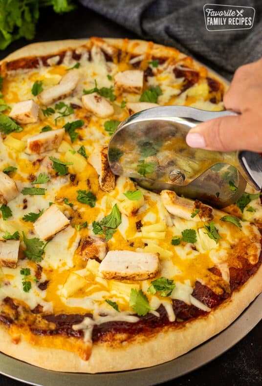 Cutting BBQ Chicken Pizza with a pizza cutter.