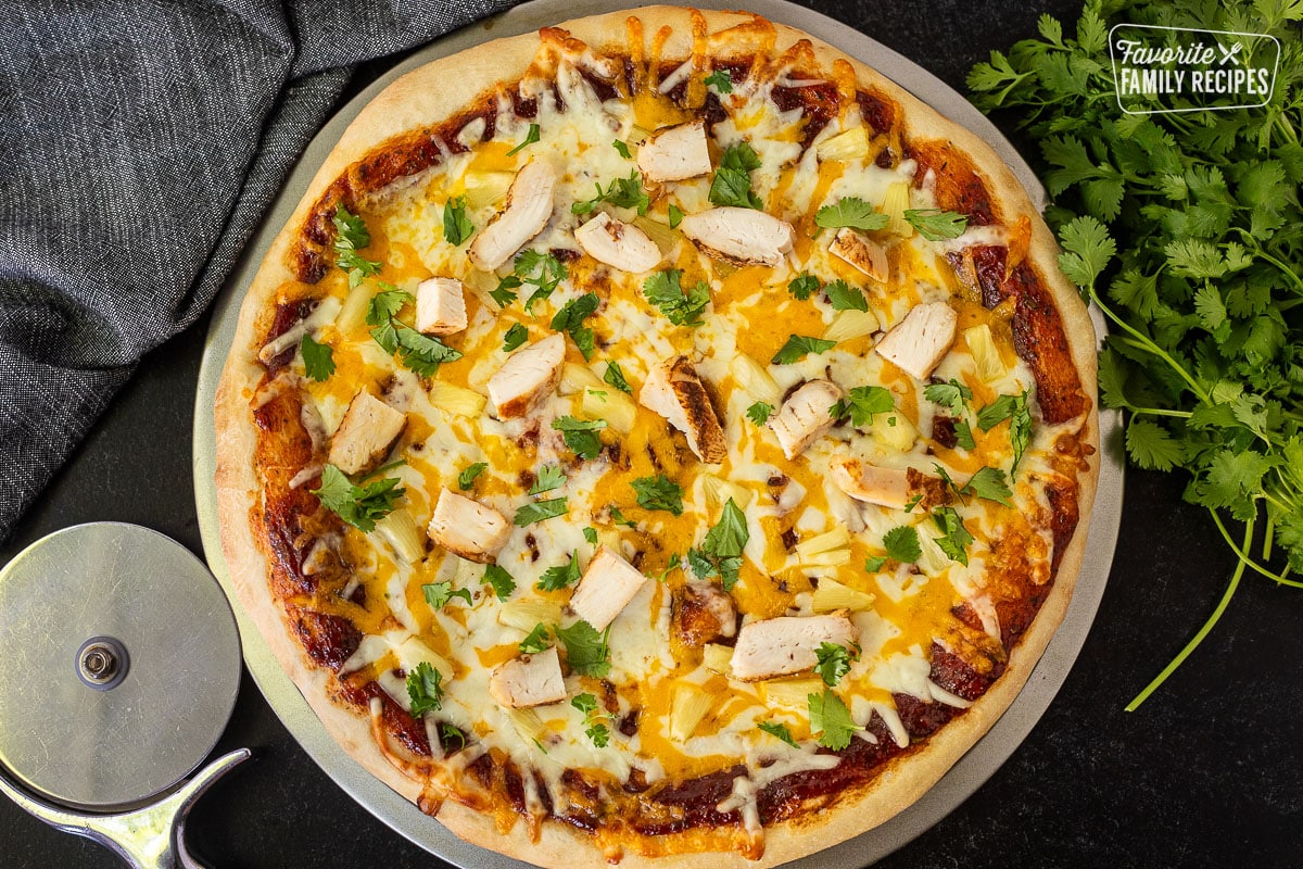 Baked BBQ Chicken Pizza on a pan with fresh cilantro. Pizza cutter on the side.