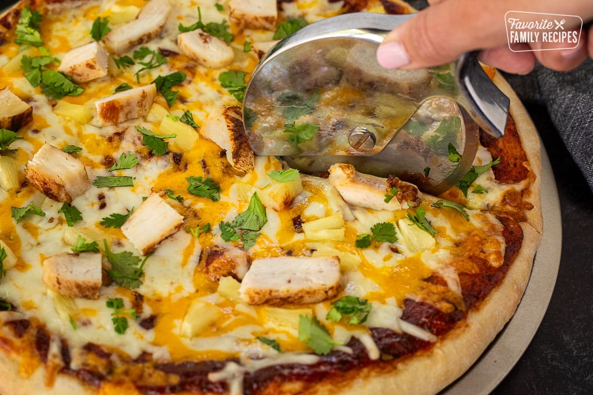 Cutting BBQ Chicken Pizza with a pizza slicer.