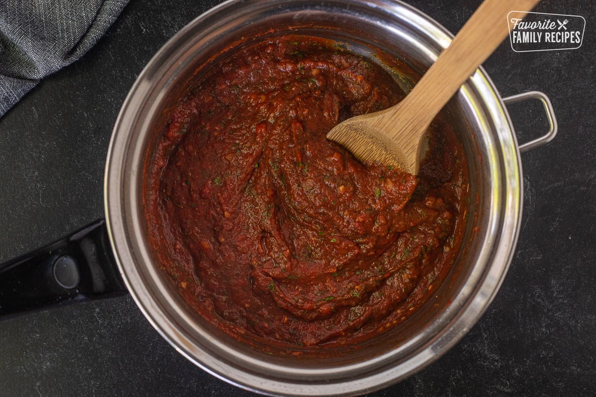 Saucepan with pizza sauce base and wooden spoon.