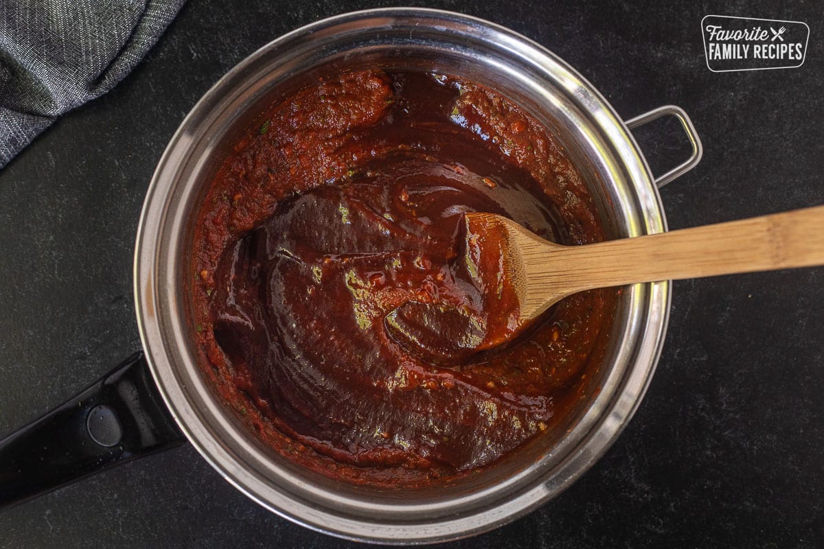 Saucepan combining pizza sauce and barbecue sauce with a wooden spoon.