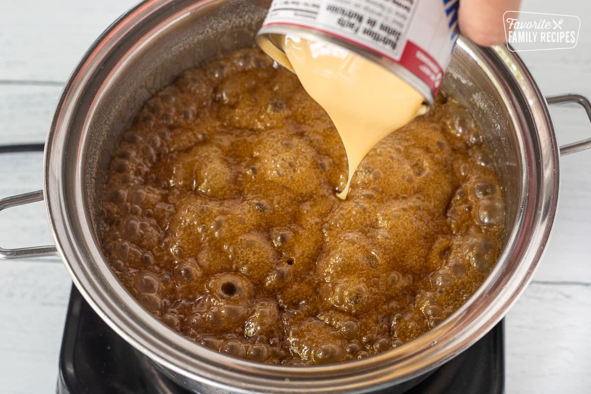 Pouring sweetened condensed milk into a saucepan of boiling caramel.