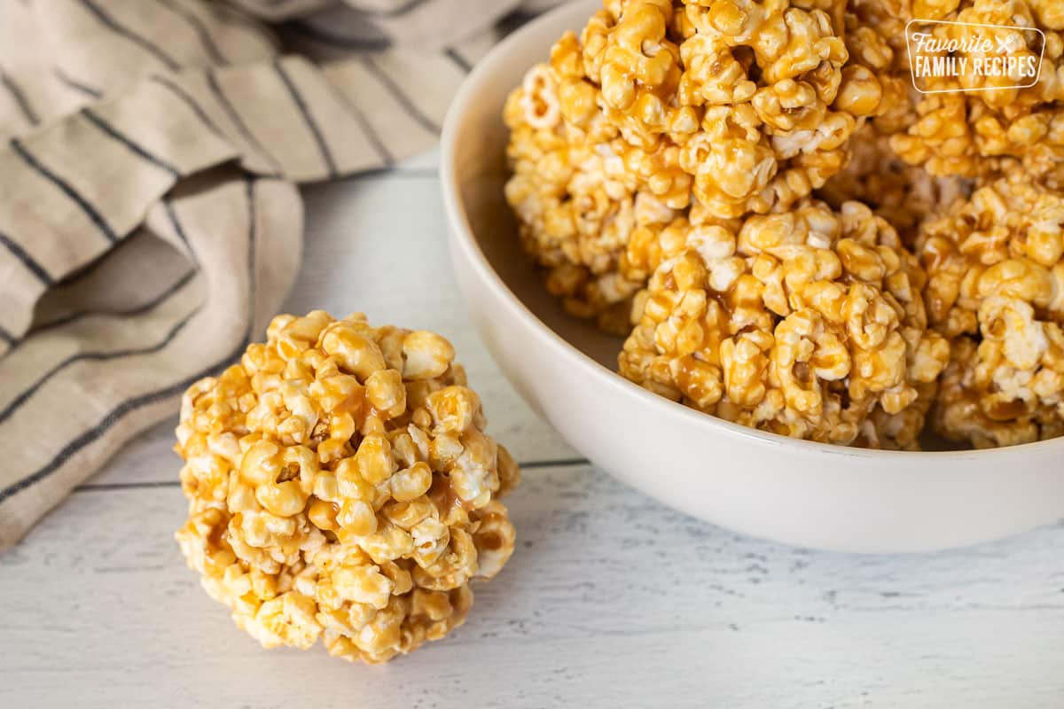 Ball of caramel popcorn next to a bowl of caramel popcorn balls.