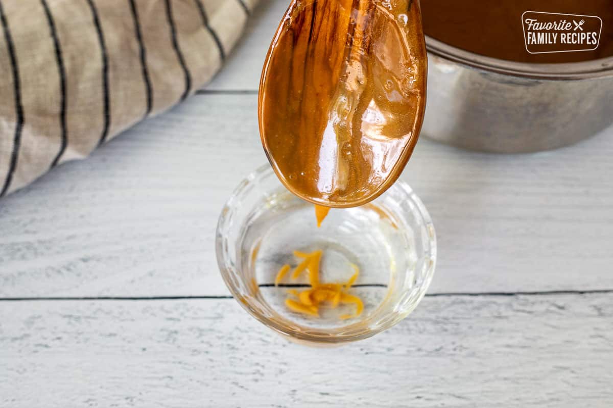 Dripping caramel into a small glass of water from a wooden spoon.