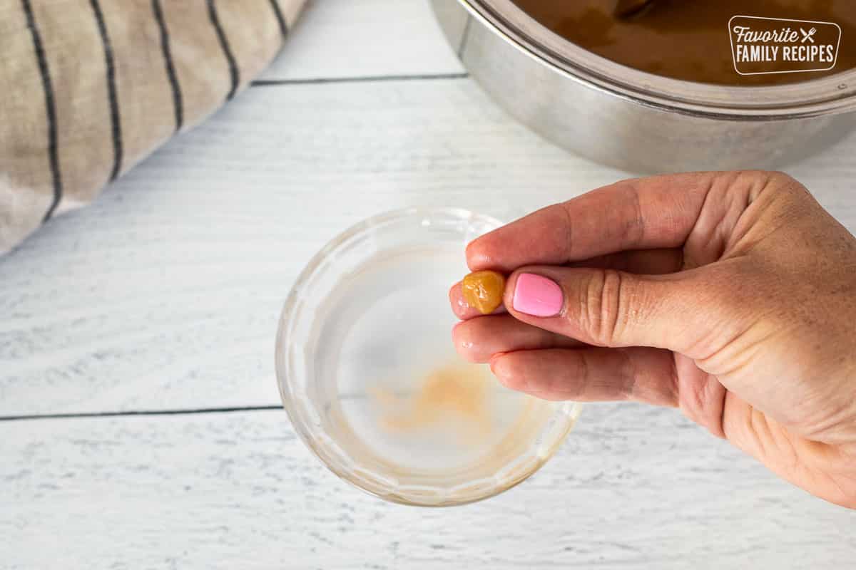 Rolling caramel into a ball in hands over a glass of water.